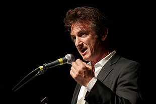 man wearing black suit jacket speaking near microphone